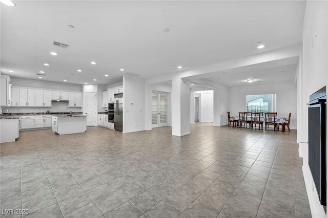 unfurnished living room with light tile patterned floors, recessed lighting, visible vents, a sink, and baseboards