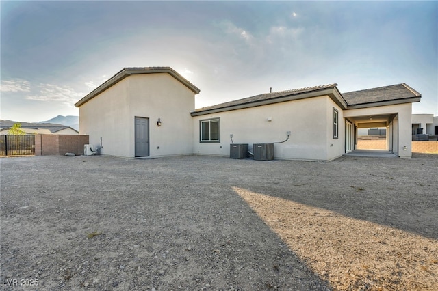 rear view of property with fence, central AC, and stucco siding