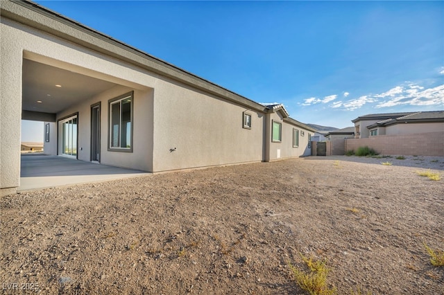 view of side of property featuring fence, a patio, and stucco siding