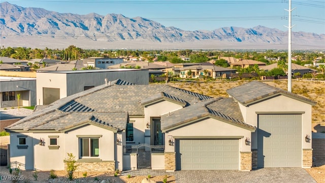 view of front of property with decorative driveway, an attached garage, a mountain view, and stucco siding