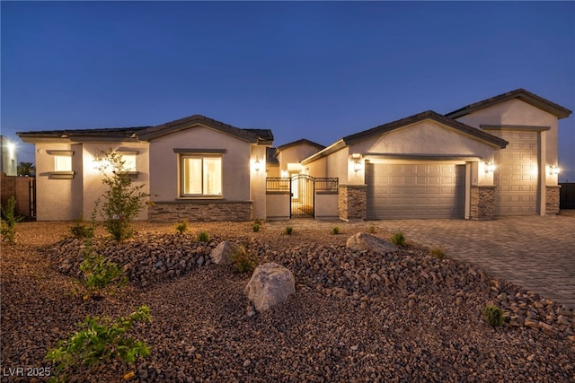 view of front of house featuring stone siding, an attached garage, a gate, decorative driveway, and stucco siding