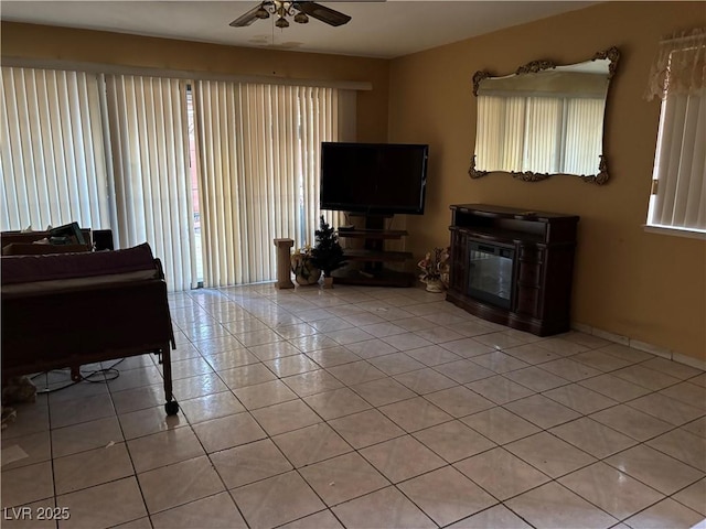 living room with a ceiling fan, a glass covered fireplace, a wealth of natural light, and light tile patterned floors