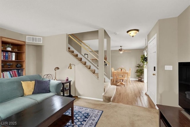 carpeted living area with stairs, ceiling fan, visible vents, and baseboards