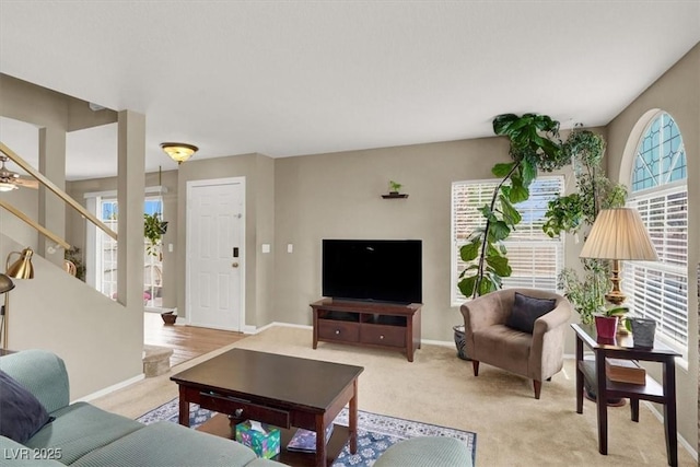 living area with stairway, baseboards, and light colored carpet