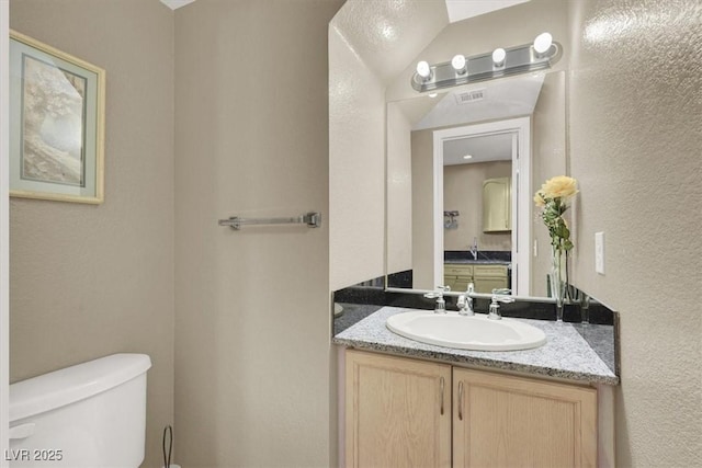 half bath featuring toilet, a textured wall, visible vents, and vanity