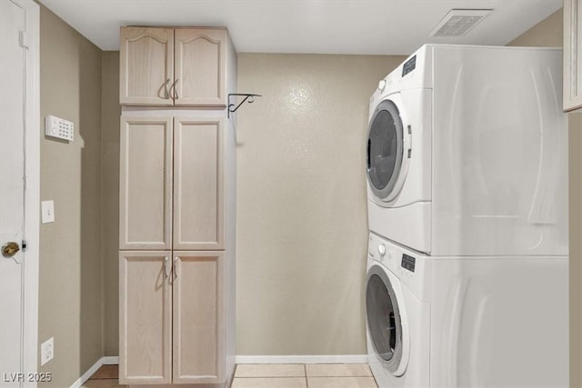 laundry area featuring visible vents, baseboards, stacked washer / drying machine, cabinet space, and tile patterned floors