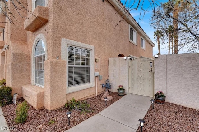 entrance to property featuring a gate, fence, and stucco siding