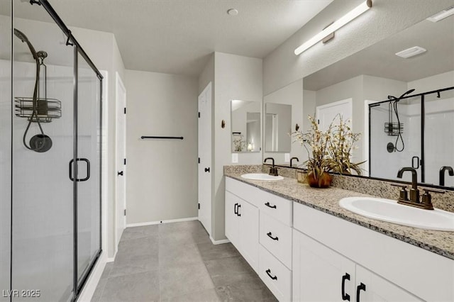 bathroom with baseboards, double vanity, a sink, and a shower stall