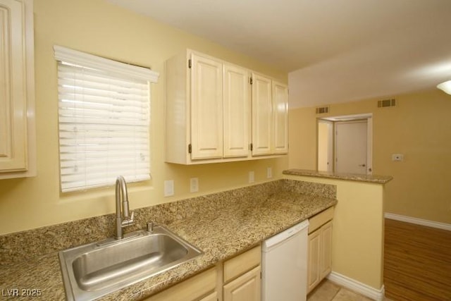 kitchen featuring baseboards, visible vents, a peninsula, white dishwasher, and a sink