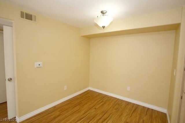 spare room featuring wood finished floors, visible vents, and baseboards