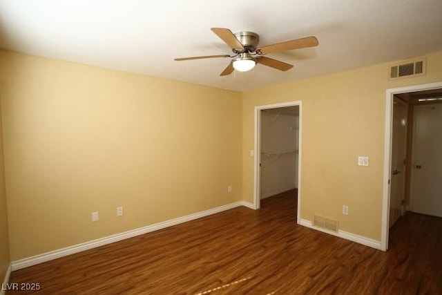 unfurnished bedroom with wood finished floors, visible vents, baseboards, a closet, and a walk in closet