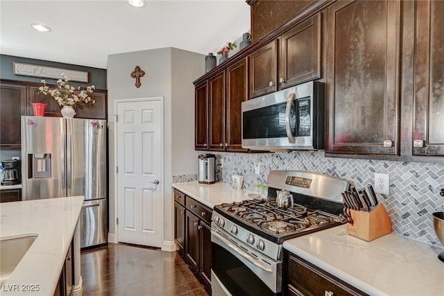 kitchen featuring dark wood-style flooring, backsplash, appliances with stainless steel finishes, dark brown cabinetry, and light stone countertops