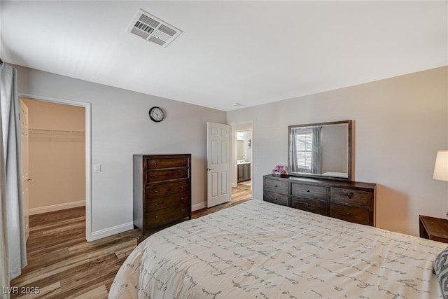 bedroom featuring wood finished floors, visible vents, baseboards, a spacious closet, and a closet