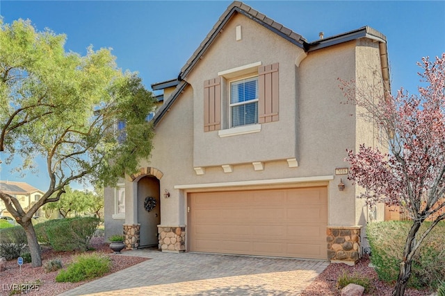 mediterranean / spanish home with an attached garage, stone siding, decorative driveway, and stucco siding