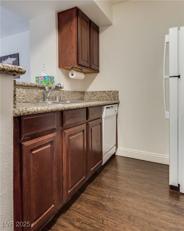 kitchen featuring white appliances, dark wood-style flooring, a sink, baseboards, and light countertops