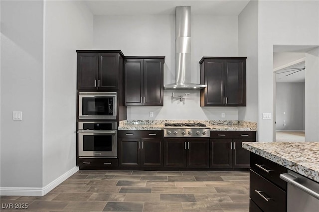 kitchen featuring wall chimney exhaust hood, appliances with stainless steel finishes, and light stone counters