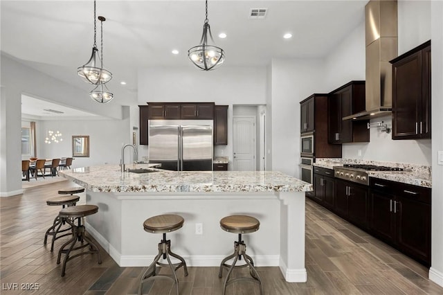 kitchen featuring visible vents, a kitchen breakfast bar, built in appliances, wood tiled floor, and a sink