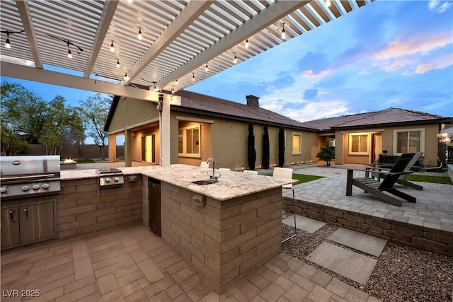 patio terrace at dusk with fence, a sink, a grill, exterior kitchen, and a pergola