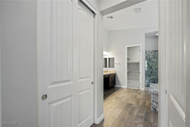 corridor with visible vents, a sink, baseboards, and wood finished floors