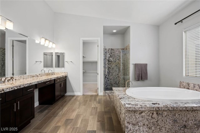 bathroom with wood finished floors, baseboards, a shower stall, a bath, and double vanity