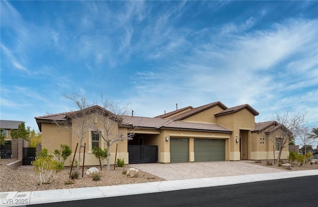 view of front of house featuring decorative driveway, stucco siding, an attached garage, a gate, and fence