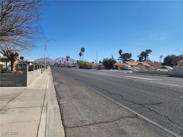 view of street with sidewalks, curbs, a mountain view, and street lights