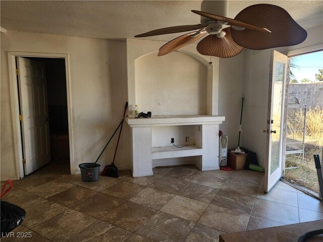 unfurnished living room featuring stone finish flooring, a ceiling fan, and a textured ceiling