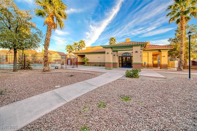 mediterranean / spanish-style home with a fenced in pool, a tile roof, fence, french doors, and stucco siding