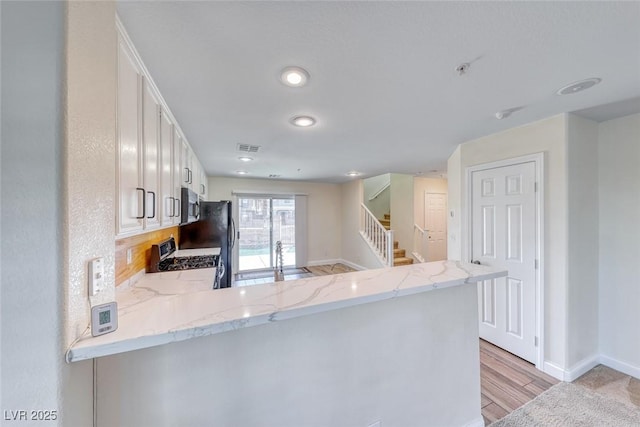 kitchen featuring range with gas cooktop, stainless steel microwave, a peninsula, light stone countertops, and a sink