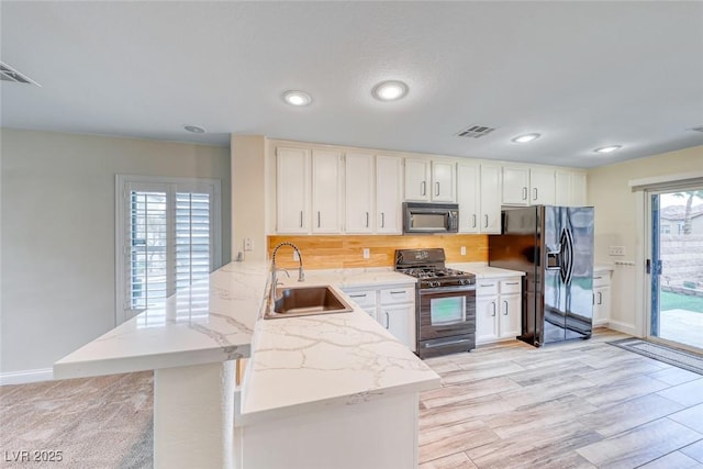 kitchen with visible vents, a peninsula, a sink, black appliances, and backsplash