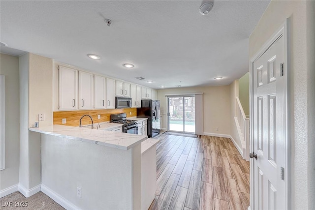 kitchen featuring range with gas stovetop, stainless steel microwave, light wood-style floors, baseboards, and black fridge