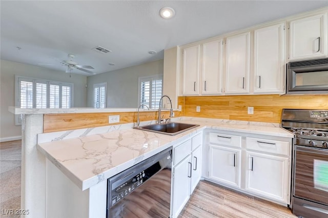 kitchen featuring visible vents, a sink, light stone countertops, a peninsula, and black appliances