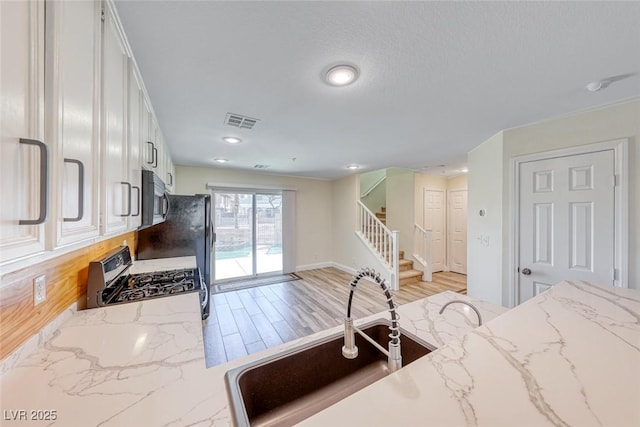 kitchen with stainless steel appliances, visible vents, light wood-style flooring, white cabinetry, and a sink