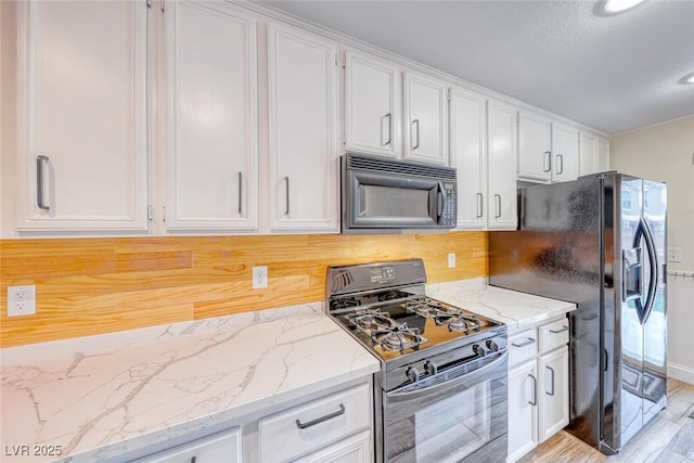 kitchen featuring black appliances, light wood-style flooring, light stone counters, and white cabinets