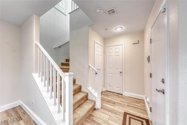 foyer featuring light wood-type flooring, visible vents, stairway, and baseboards