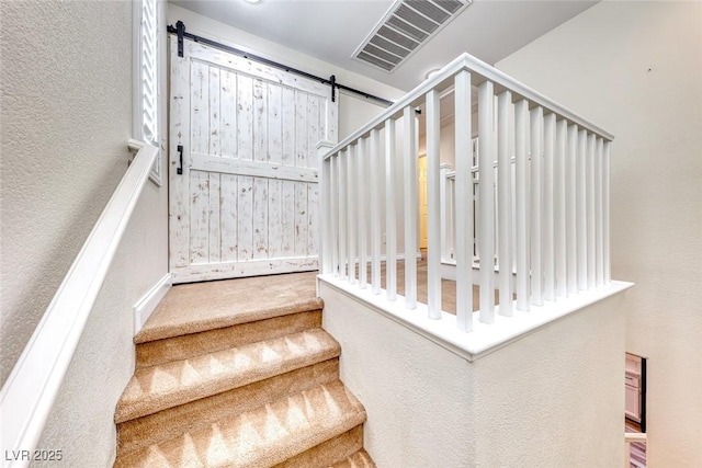 stairway with a barn door, visible vents, and a textured wall