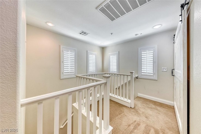 hallway featuring visible vents, a barn door, light carpet, and an upstairs landing