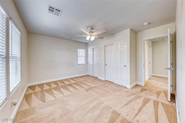 unfurnished bedroom with visible vents, light carpet, baseboards, and two closets