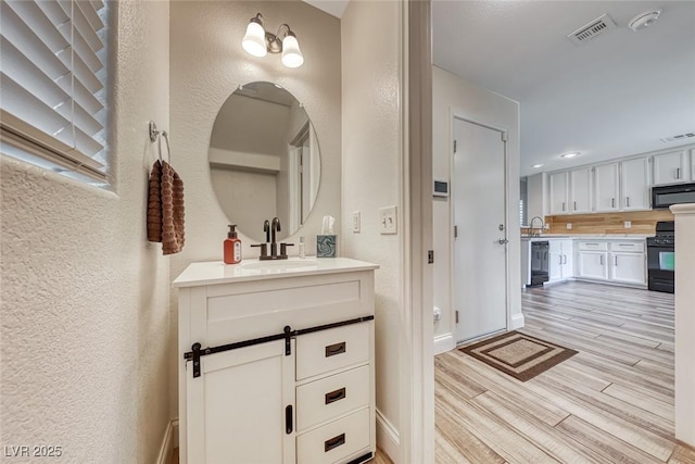 bathroom with vanity, visible vents, wood finished floors, and a textured wall