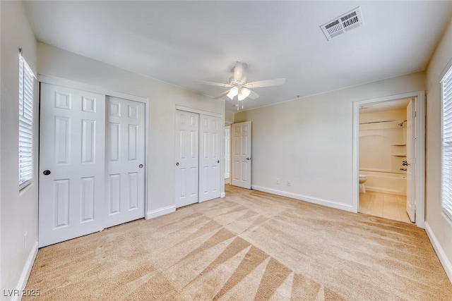 unfurnished bedroom featuring baseboards, carpet, visible vents, and multiple closets