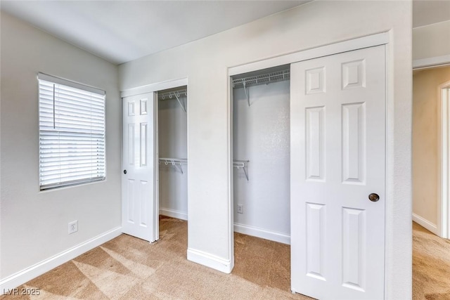 unfurnished bedroom featuring light carpet, two closets, and baseboards