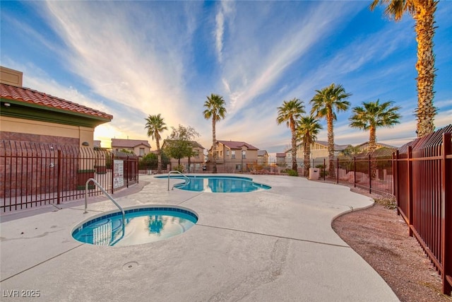 pool at dusk featuring a hot tub, a community pool, a fenced backyard, and a patio