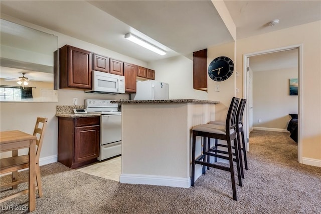 kitchen with a breakfast bar area, light carpet, a peninsula, white appliances, and a ceiling fan