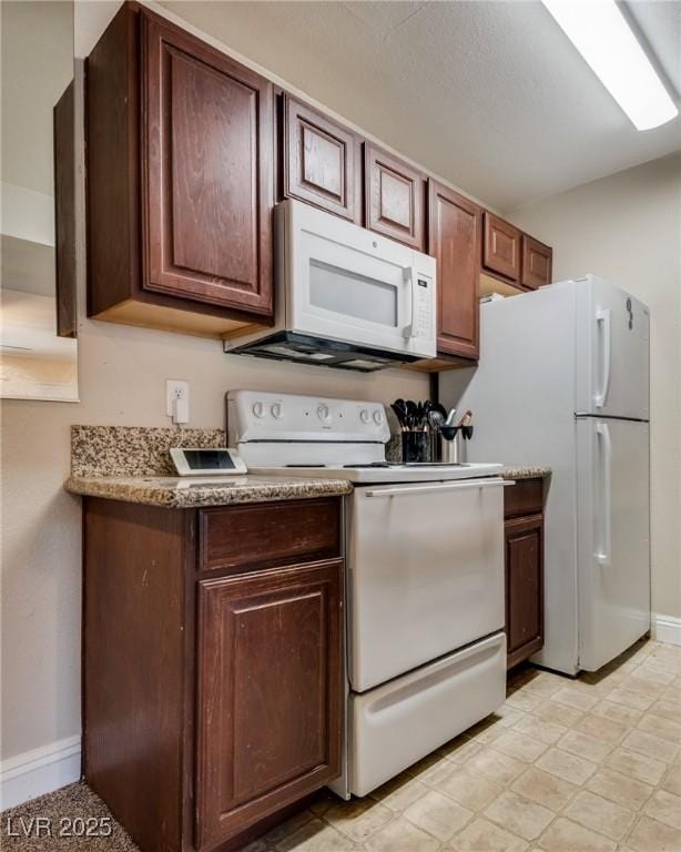 kitchen featuring light floors, white appliances, dark brown cabinets, and baseboards