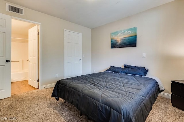 carpeted bedroom featuring ensuite bath, visible vents, and baseboards