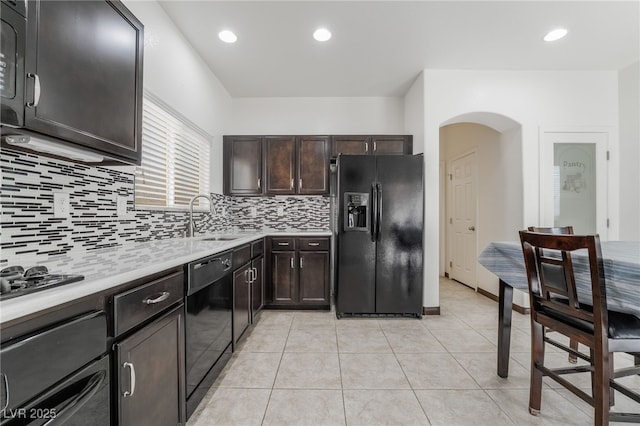 kitchen featuring light tile patterned floors, arched walkways, light countertops, black appliances, and a sink