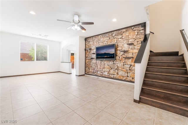 unfurnished living room featuring baseboards, arched walkways, ceiling fan, stairway, and tile patterned flooring