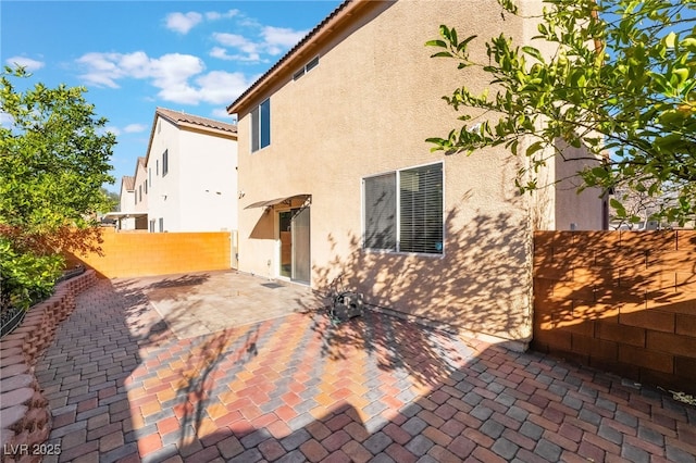 rear view of house with stucco siding, fence, and a patio