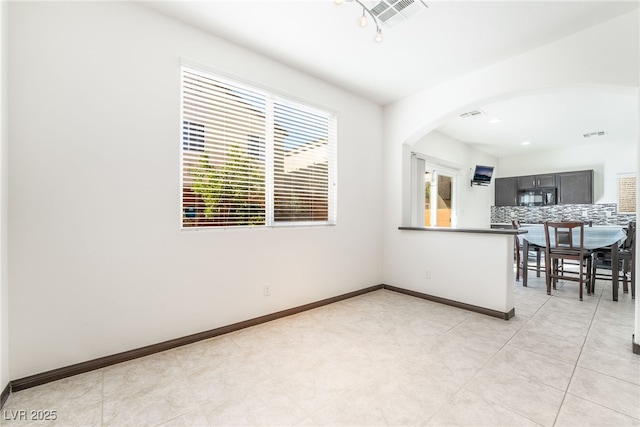 kitchen featuring black microwave, backsplash, arched walkways, and baseboards