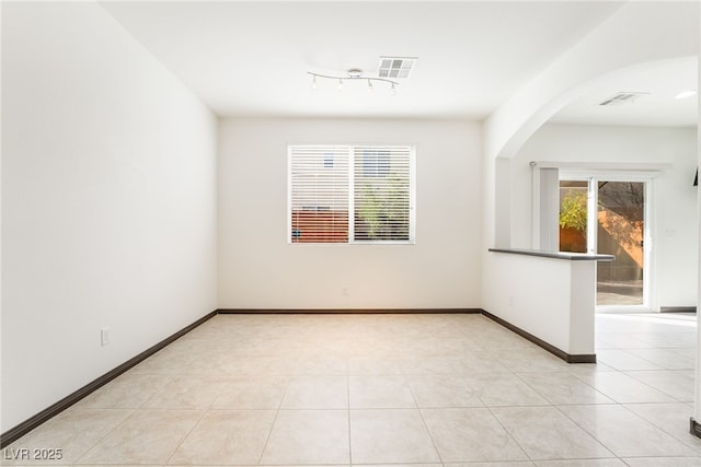 spare room with light tile patterned floors, arched walkways, visible vents, and baseboards